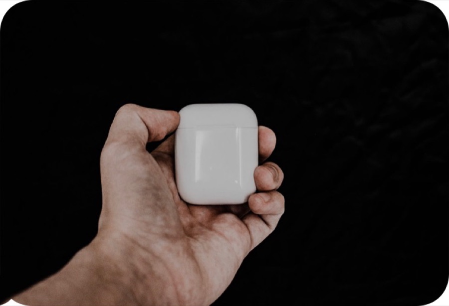 A hand holding a small white earbuds case